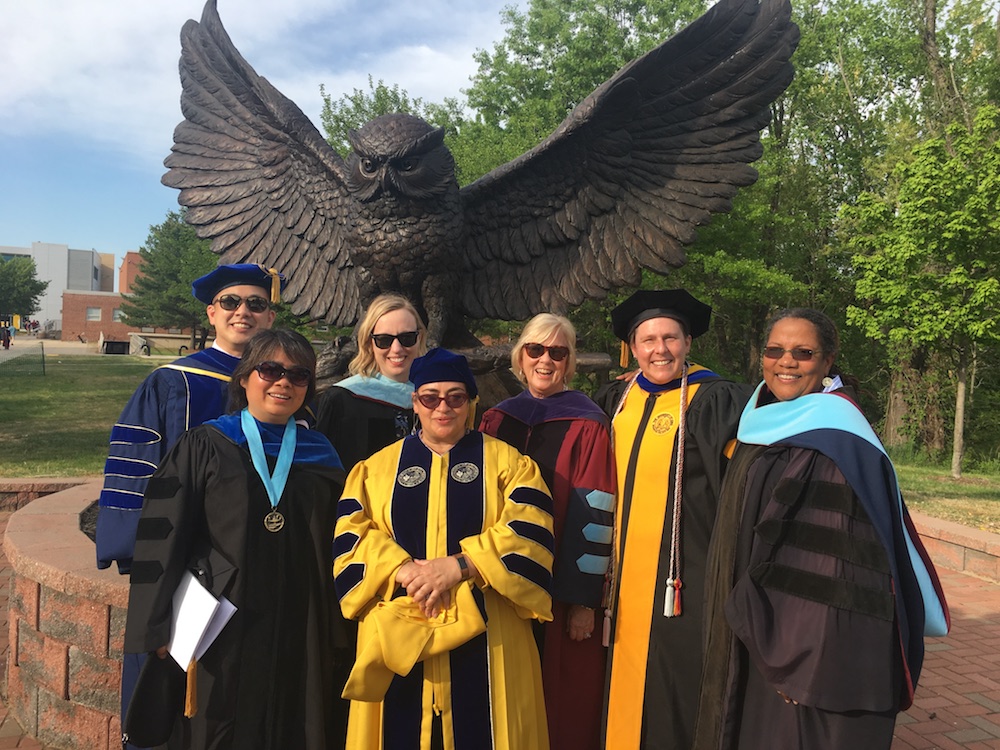 faculty members in their graduation gowns in front of the owl statue
