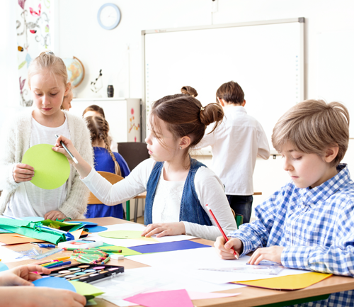 Three children work at a table using writing materials. 