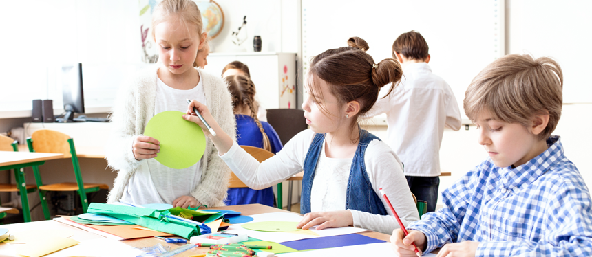  Three children work at a table using writing materials.