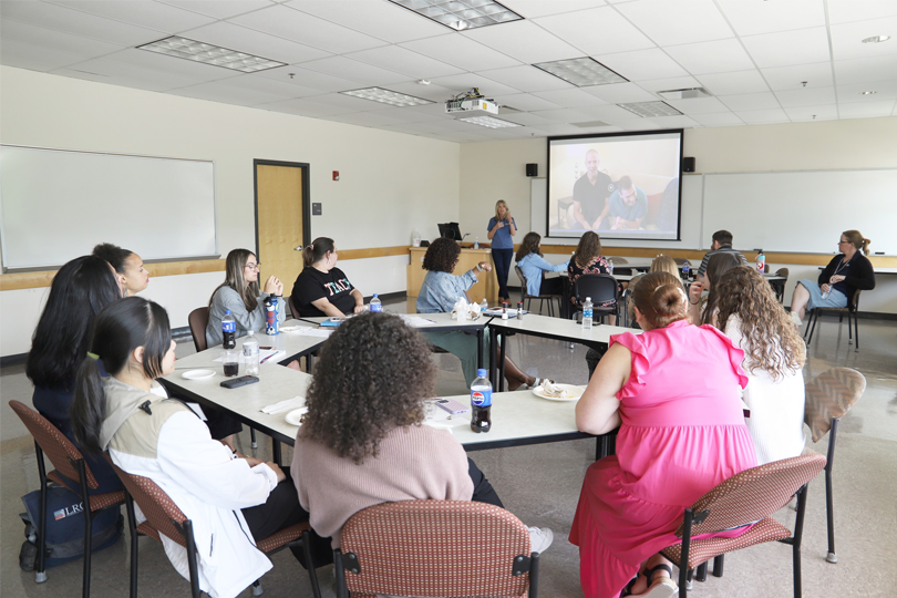 LRC-S Director, Jenny Murphy, speaks to fourteen new teacher academy participants who are seated at tables. 