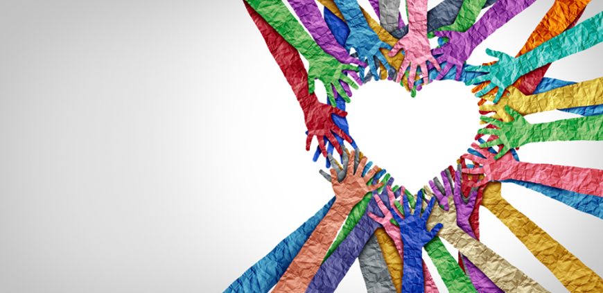 A vibrant banner image featuring dozens of multi-colored arms and hands with a crumpled paper texture reaching inward. The hands overlap and arrange themselves to outline a large, clear heart shape in the negative space against a clean, light grey background.